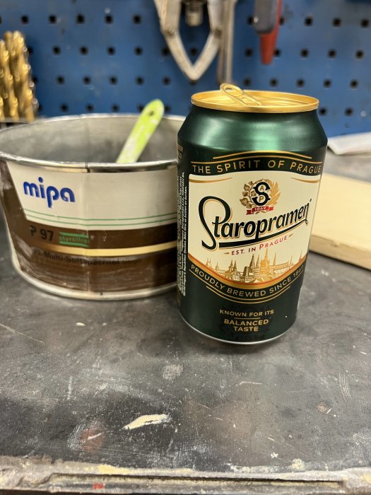 En burk Staropramen öl på ett verktygsbord i garaget med en färgblandningshink i bakgrunden.