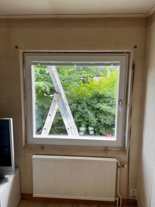 Nymonterat fönster i rum med synlig stege utanför och en radiator under fönstret.