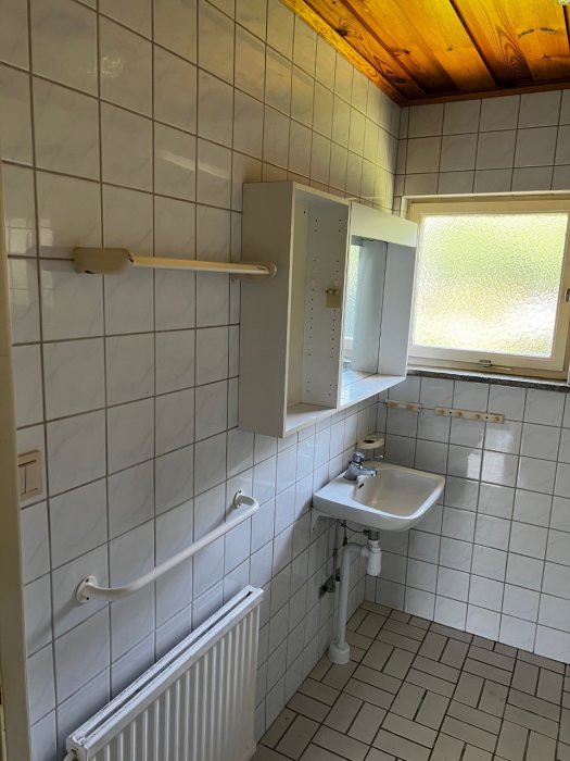 Före-rivning bild av ett badrum med vita väggar, handfat, spegel och radiator.
