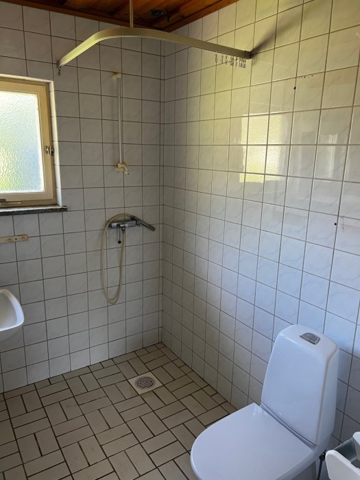 Ett badrum innan rivning med kaklade väggar, dusch, toalett och handtag på väggen.