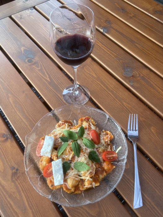 Tallrik med burkravioli dekorerad med basilika och ost, serverad med ett glas rödvin, på ett träbord.