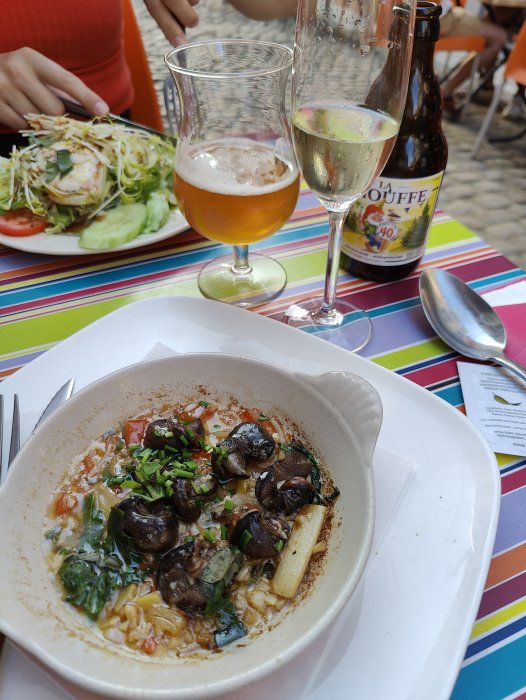 En skål med sniglar och grönsaker, ett glas öl, ett glas champagne och en sallad i bakgrunden.