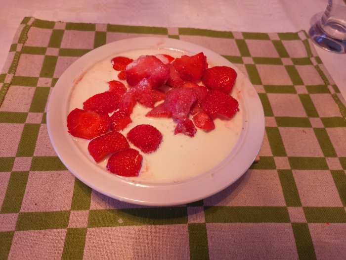 Skivade jordgubbar i skål med grädde på en grön- och vitrutig duk.