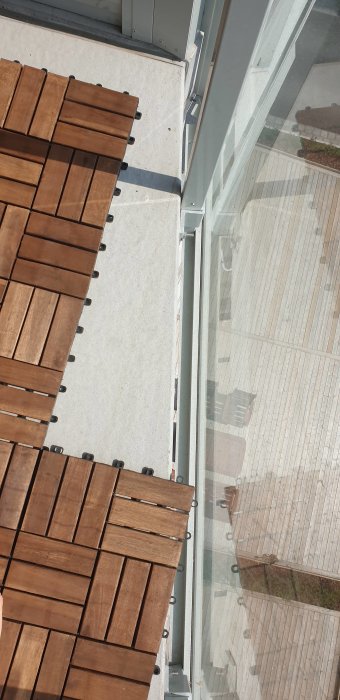 Utlagt trätrall vid balkongkant som skapar en vinkel mot glasräcket, sågning behövs för anpassning.