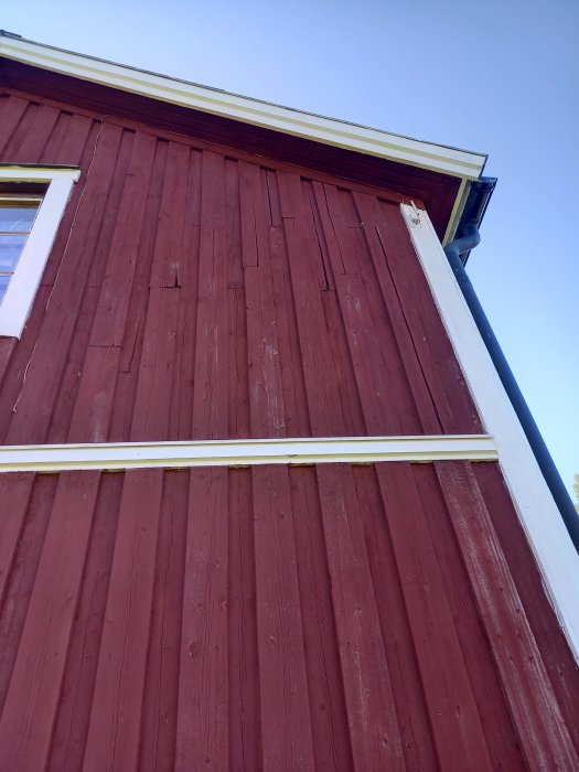 Rödmålad träfasad på hus med synlig slitage och sprucken färg, fråga om täckning med latex.