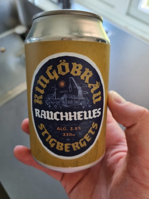 Hand håller en burk med folköl märkt "Rauchelles" från Stigbergets Bryggeri, alkoholhalt 3,5%.