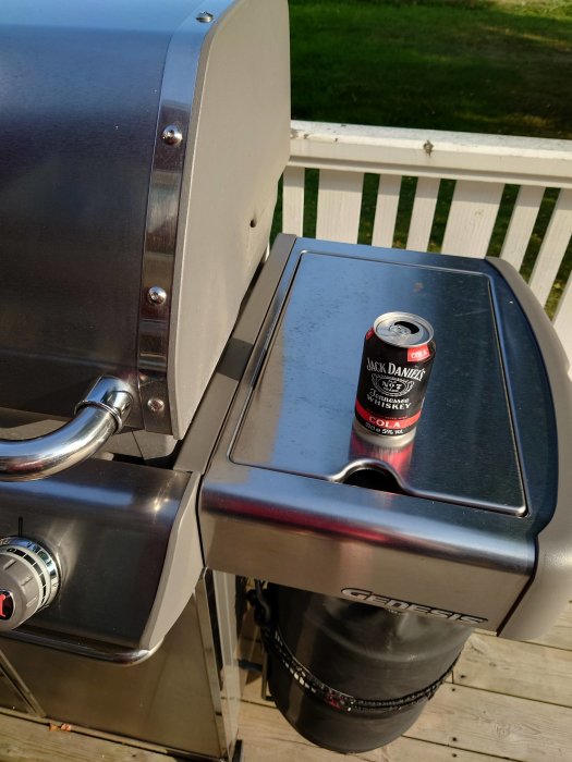 En burk Jack Daniel's med Cola står ovanpå en gasolgrill på en träaltan.