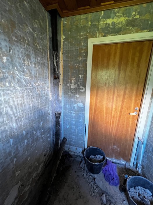 Renoveringsarbeten i badrum med bilade väggar och avloppsrör synligt, samt hinkar med rivningsmaterial.