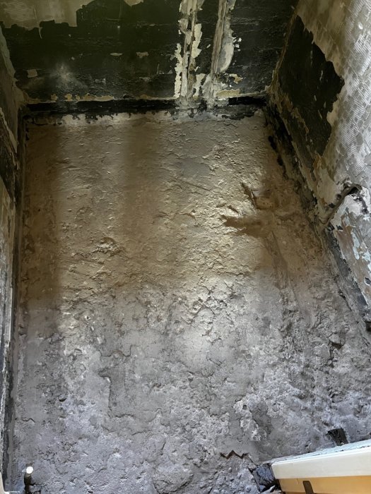 Ett delvis bilat badrumsgolv och nedrivna väggmaterial synliga i en renoveringsskede.