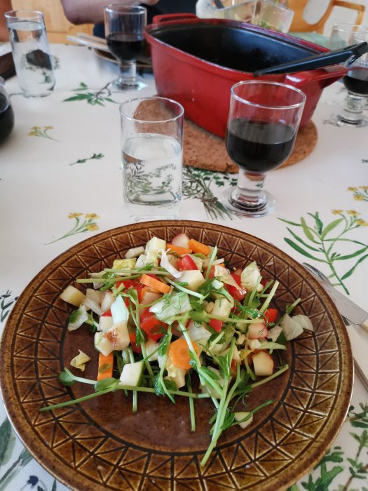 Färgrik sallad med tärnade grönsaker, äpple och nektarin på brun tallrik med glas och vin.