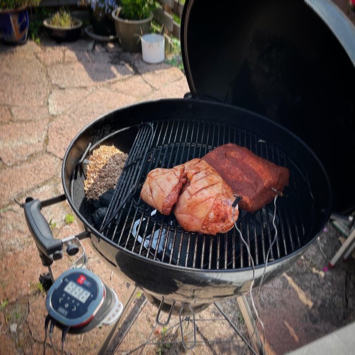 Grill med två stycken köttbitar, en trådlös termometer vid sidan, på en stenlagd uteplats.