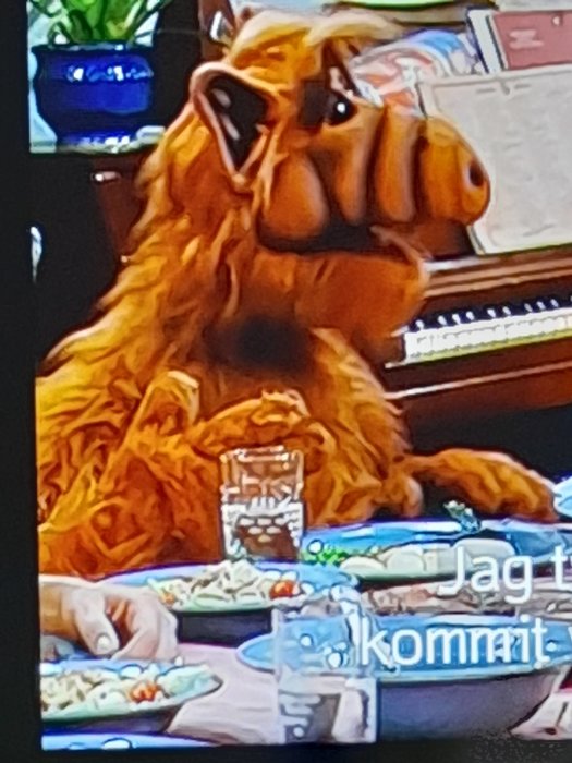 Dockan ALF från en 80-talsserie sitter vid ett bord med maträtter framför sig.