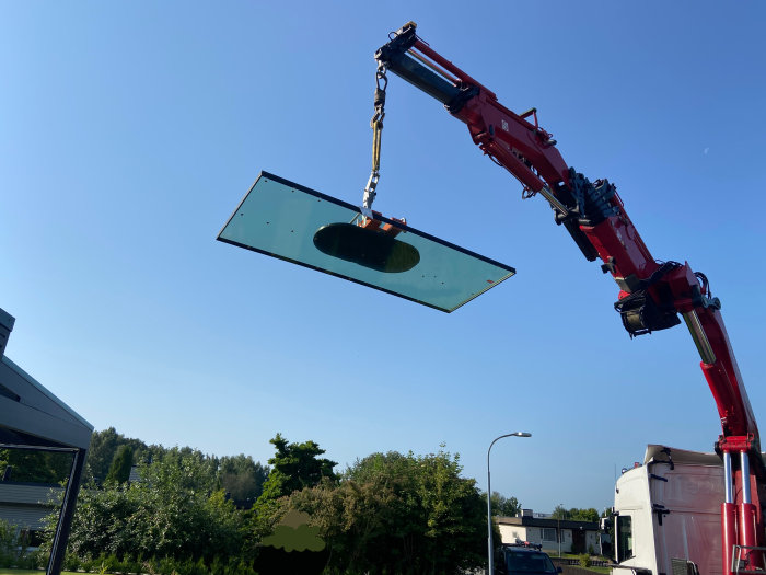 Ett stort glasfönster lyfts med en mobilkran mot en klarblå himmel.