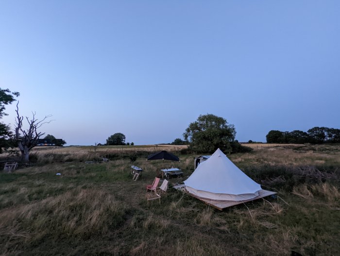 Campingplats med tält och utemöbler i skymningen på en gräsmark.
