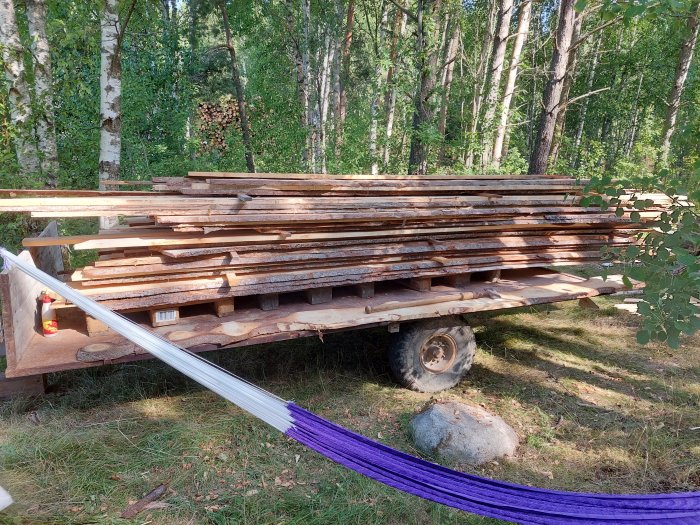 Stapel av vildmarkspanel på en vagn i en skogsmiljö som väntar på att behandlas och monteras.