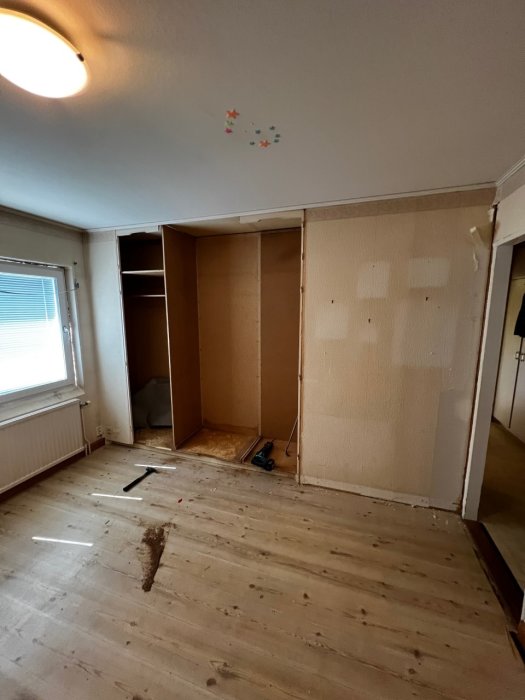 Rivningsarbete av en inbyggd garderob i ett rum, med verktyg på golvet och öppna garderobsdelar.