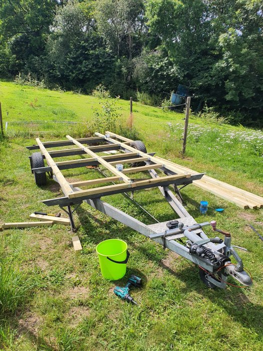 Impregnerade träreglar monterade på en husvagnschassi utomhus som grund för en bastubyggnad.