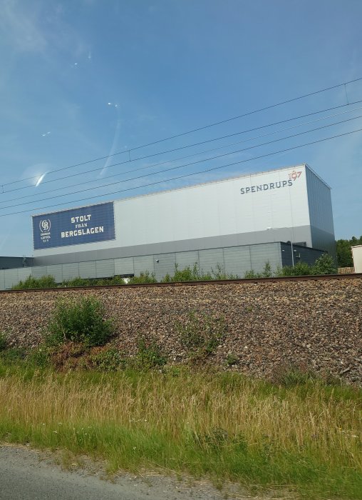 Stort industriellt lagerhus med logotypen Spendrups och texten "STOLT FRÅN BERGSLAGEN" på sidan, sett från vägen.