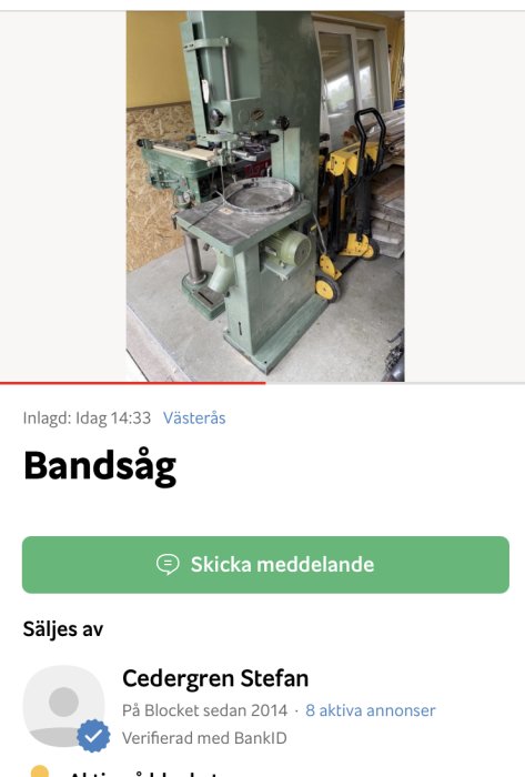 Stor och gedigen grön Meber bandsåg i ett garage, utan angivet pris.