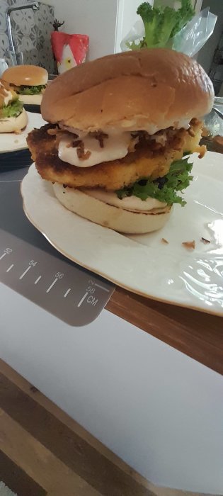 Kycklingburgare med panerad kyckling, sallad och sås mellan två brödhalvor på en vit tallrik.