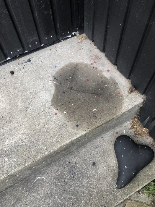 Stearinfläck på betongtrappa med omkullvält svart hjärtformat ljus och små stearinbitar.