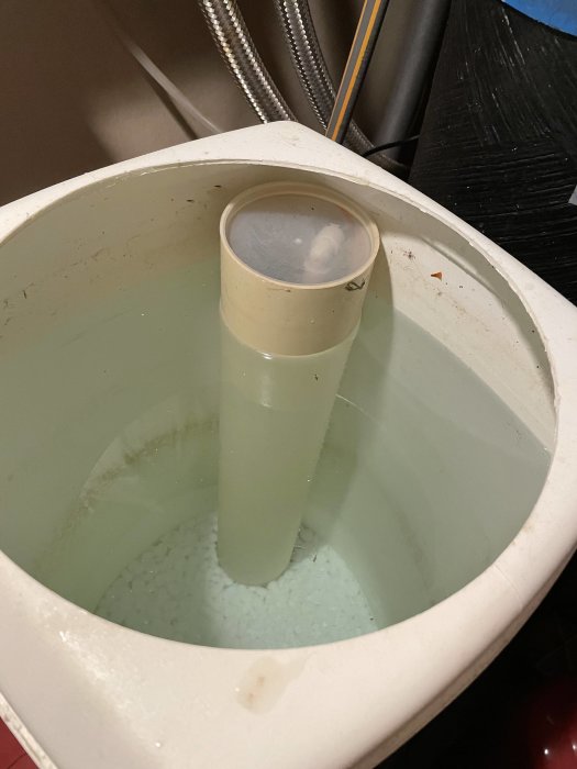 Översvämmad saltbehållare i en avkalkningsmaskin med lite synligt salt i botten och vatten upp till kanten.