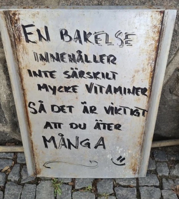 Gammal skylt med texten "En bakelse innehåller inte särskilt mycket vitaminer så det är viktigt att du äter många".