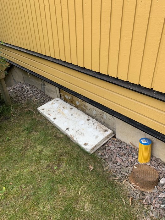 Grund av hus med gul panel, en vit betongplatta och brun färg som flagnar nära marken.