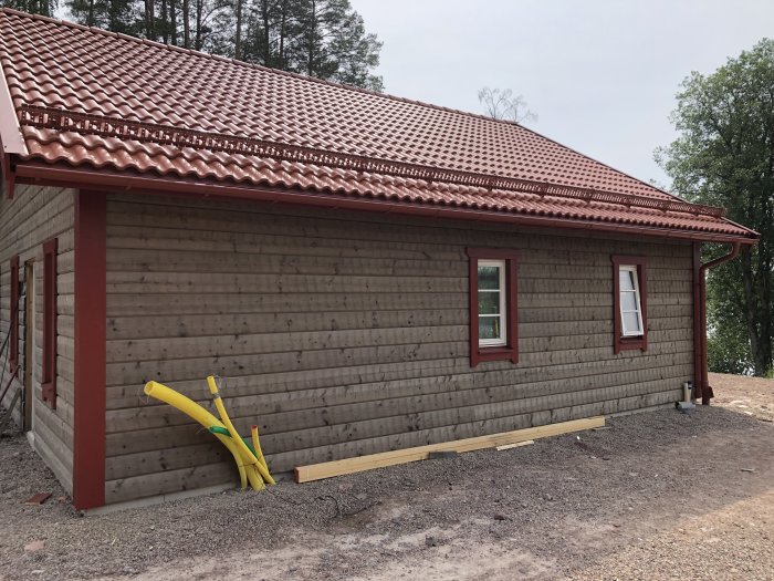 Ett hus under renovering med nymålade vindskivor och röda fönsterfoder utan hängrännor.