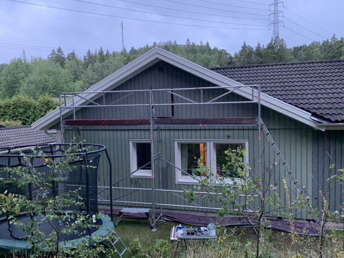 Renoverat hus med nymålade vindskivor, takfot och vindslucka, byggnadsställningar runt fasaden.