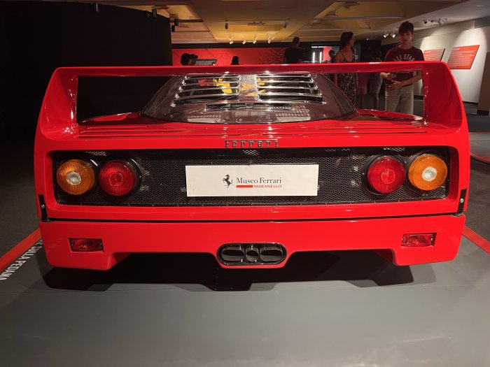 Bakifrånvy av en röd Ferrari utställd på Museo Ferrari Maranello med besökare i bakgrunden.