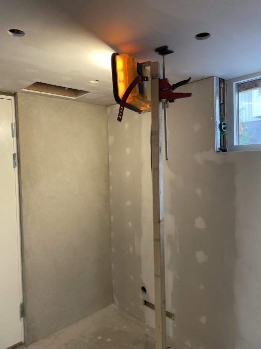 En ofärdig vägg med synlig spackling och en värmelampa monterad på en ställning som torkar spacklet.
