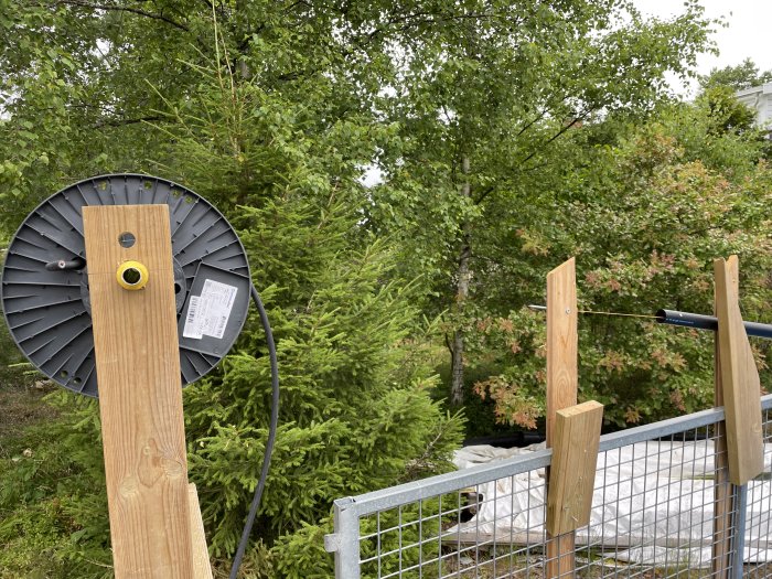 En hemmagjord träställning med en kabel som löper genom en gul kabelhållare, bakgrunden visar gröna träd och en parabolantenn.