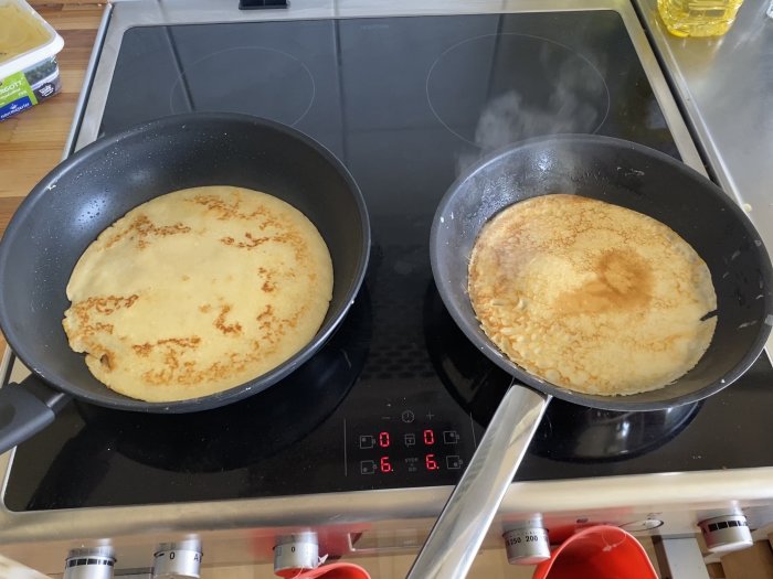 Två stekpannor med pannkakor på en spis med induktionshäll.