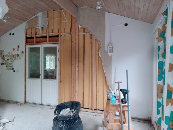 Renoveringsarbete med borttagen gipsskiva som avslöjar trästommen och isoleringen i ett rum.