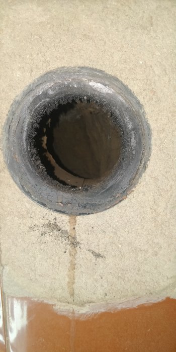 Öppning av en avloppsrör i betonggolv med synlig rörkant och del av kakel.