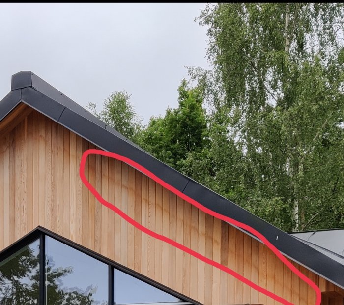 Del av modern husfasad med träpanel och svart takkant, röd cirkel markerar område.