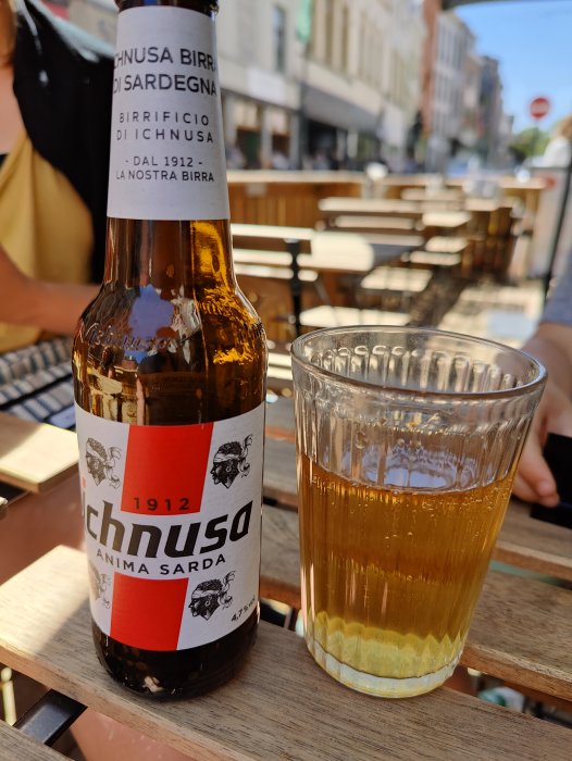 Ichnusa italiensk lageröl i flaska och glas på ett cafébord utomhus.