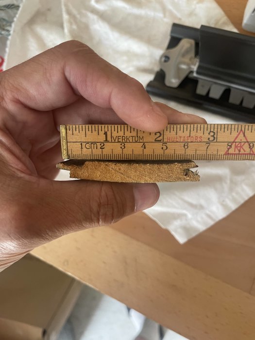 Hand håller ett måttstock mot ett trästycke för att visa dess tjocklek.