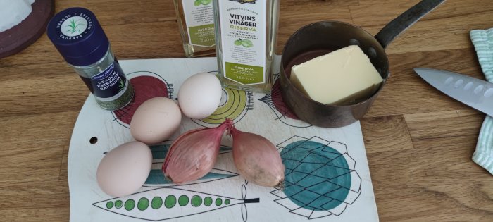 Ingredienser för matlagning på köksbänk, inklusive ägg, schalottenlök, dragonkrydda, vitvinsvinäger och smör.