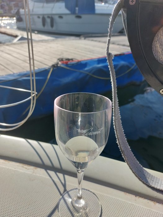 Vin i glas märkt "Yacht" på en båts fördäck, rep och annan båt i bakgrunden.