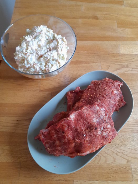 Råa kryddade babyribbs på fat bredvid en skål med coleslaw på ett träbord.