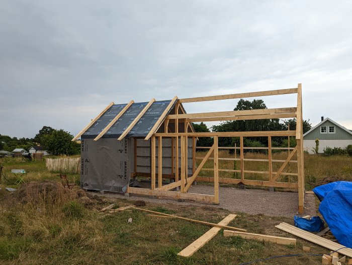 Stomme av trähus under uppbyggnad med vindduk och underlagstak installerat på ena halvan.