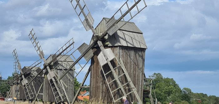 Gamla trävindkraftverk i ett landskap under blå himmel, illustrerar historiskt byggnadsskick.