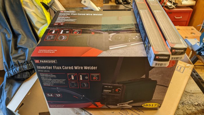 Oöppnad förpackning av en Parkside Inverter Flux Cored Wire Welder i ett verkstadsutrymme.