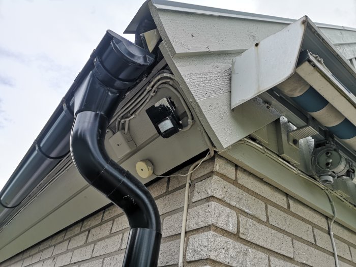 Stupränna i svart plast leder ned till en samlares vattentunna på en husfasad med tegel och vitt trä.