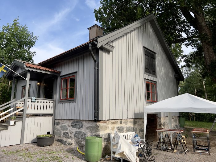 Renoverat grått hus med engelskt röda fönsterbågar, svart dörr och pågående målningsarbete.