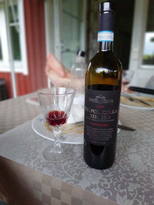 Flaska röd Valpolicella Ripasso vin på bord med ett glas vin och rester av en måltid i bakgrunden.