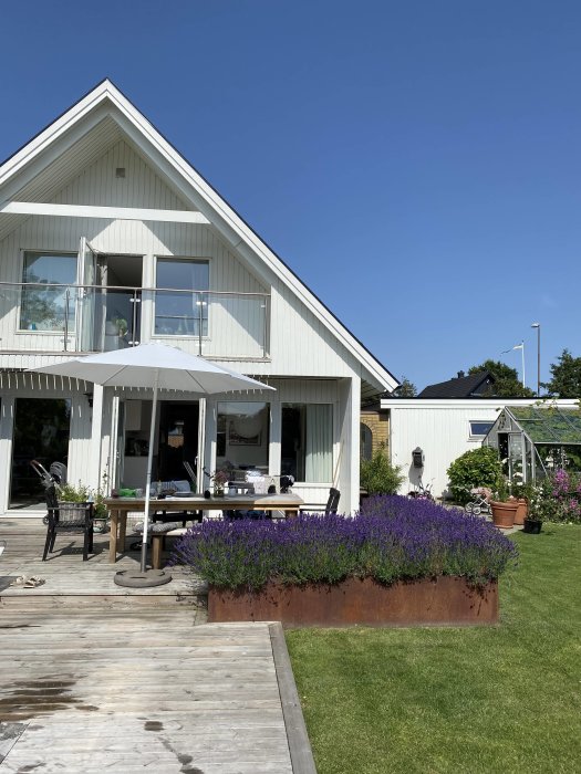 Vit villa med spetsigt tak, altan och lavendelplantering i blom mot klarblå himmel.