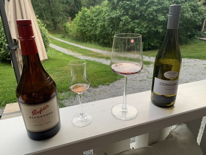 Flaska av Penfolds Grand Tawny bredvid ett grappa-glas och Stoneleigh Pinot Noir på en veranda.